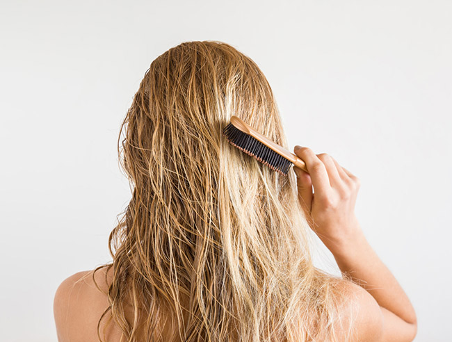 An image showing a woman combing her wet hair using a hair brush